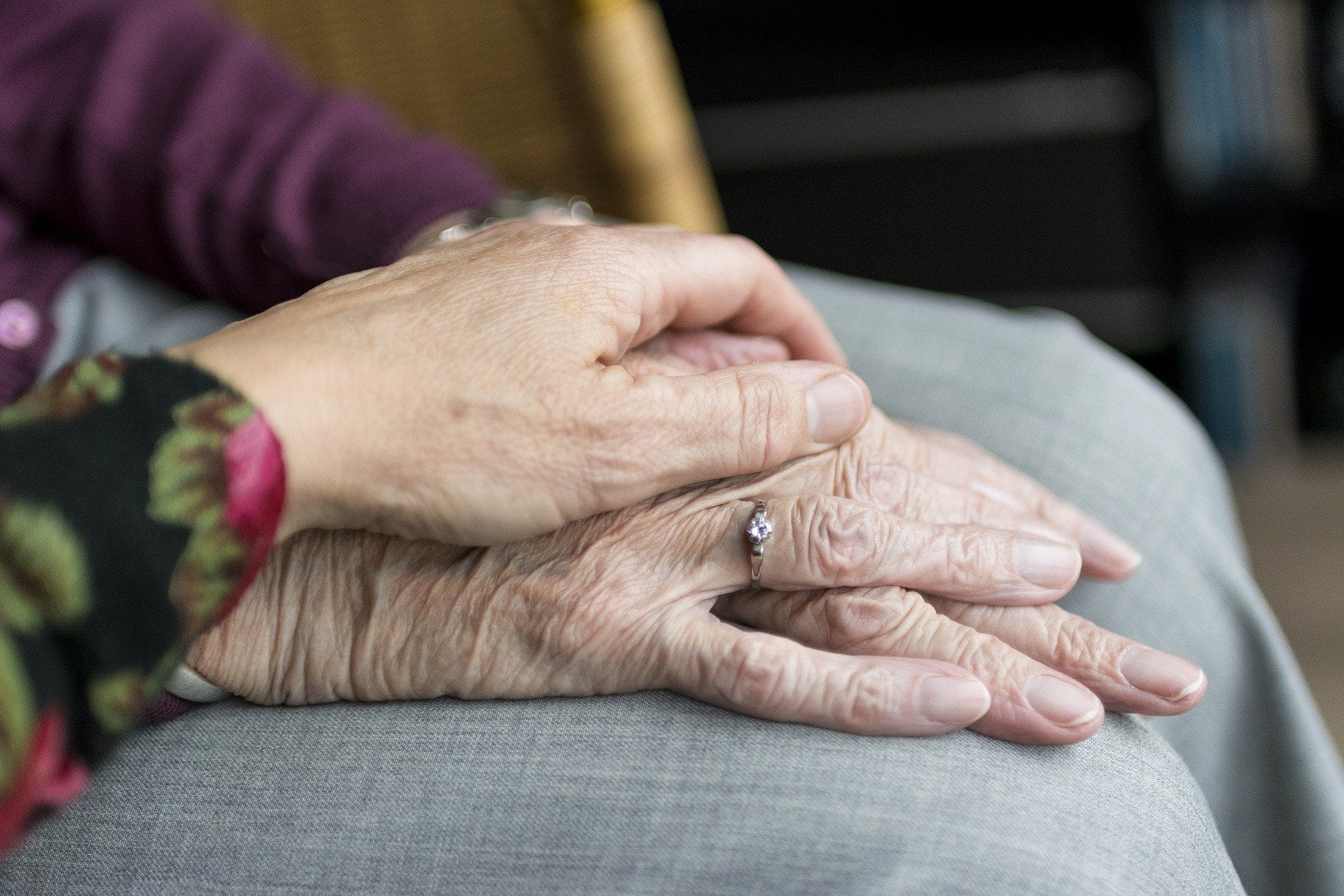 Two elderly residents hands clasped over together